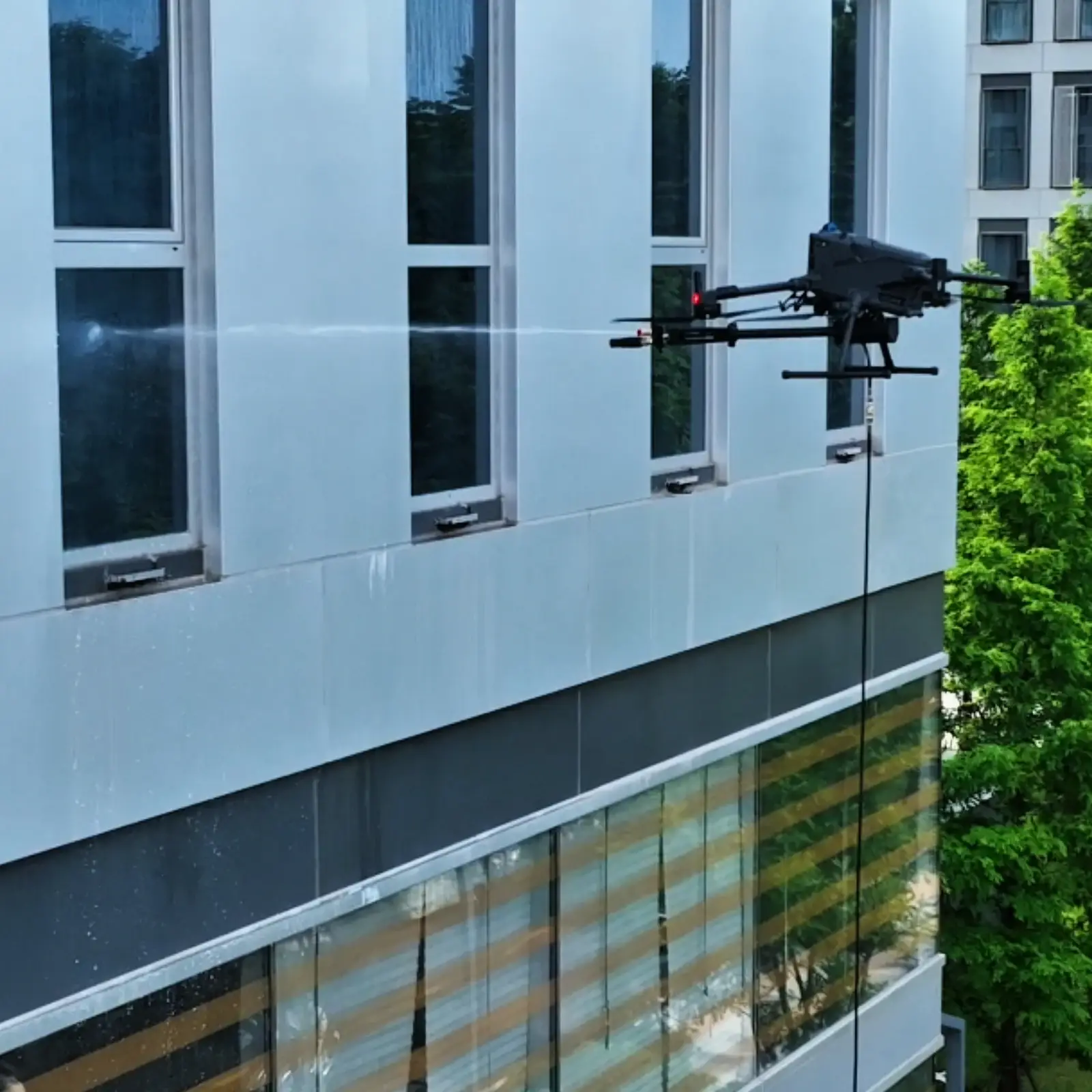 SkyFlow HoverWash 3 cleaning payload operating beside a modern facade